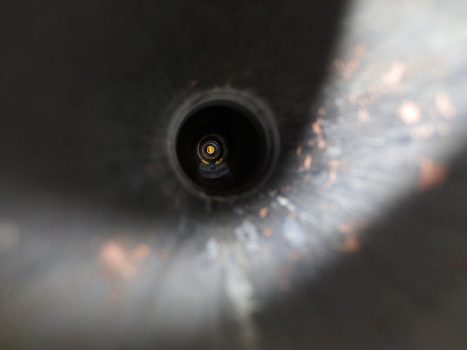 Close-up view into a dark, metallic exhaust pipe opening with a yellow reflection visible inside