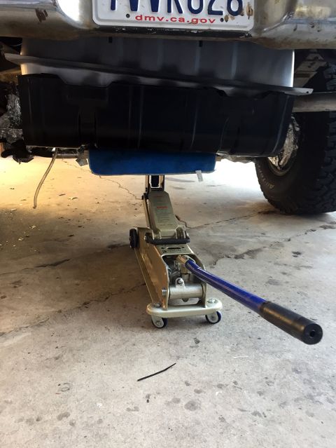 1978 Ford Bronco - A floor jack is holding up the fuel tank of a vehicle, likely for maintenance or repair.