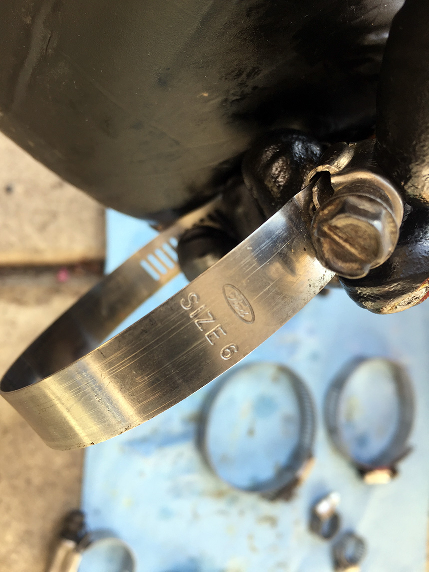 Metal hose clamp with 'SIZE 6' and Ford logo stamped on it, with other clamps blurred in background
