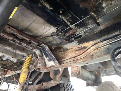 1978 Ford Bronco - The underside of a vehicle shows significant rust and exposed mechanical components.