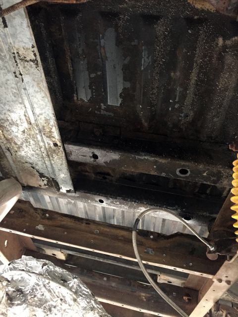 1978 Ford Bronco - The underside of a vehicle shows extensive rust and wear on its frame and body panels.