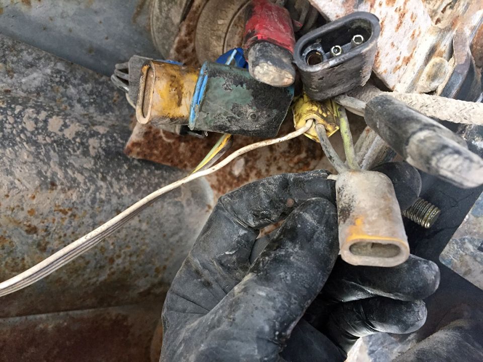 Close-up of corroded electrical connectors and wiring, held by a gloved hand