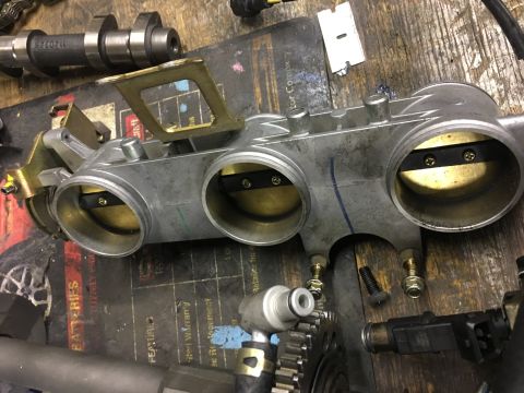 2000 Ford E350 - A disassembled throttle body with visible butterfly valves and associated sensors, resting on a workbench.