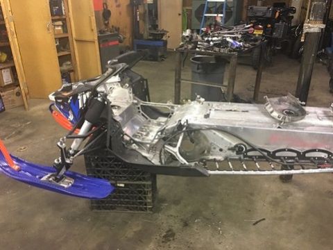 2000 Ford E350 - The main frame of a snowmobile is elevated on black crates in a garage setting, awaiting repair or reassembly.