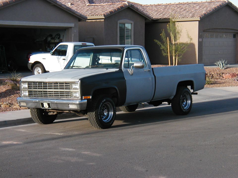 Lifted two-tone gray-and-black square-body Chevy pickup, front 3/4 on a street