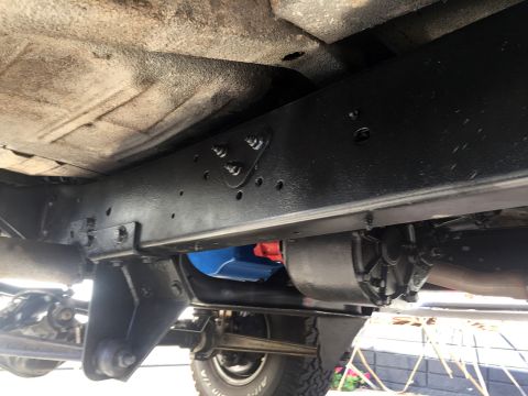 1978 Ford Bronco - Underbody view of a refinished black truck frame rail with a blue-painted fuel tank and rear axle/suspension components.