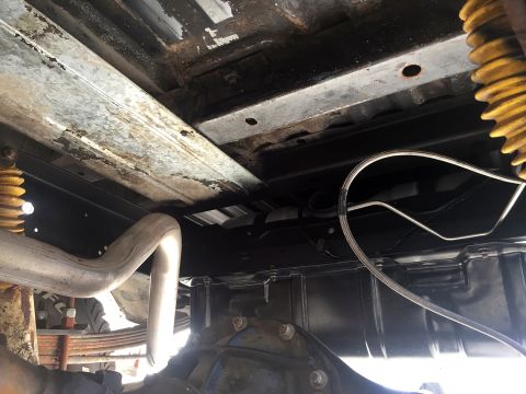 1978 Ford Bronco - Underside view of a vehicle showing the frame rail, exhaust pipe, leaf spring, yellow coil shocks and rear axle, with surface rust.