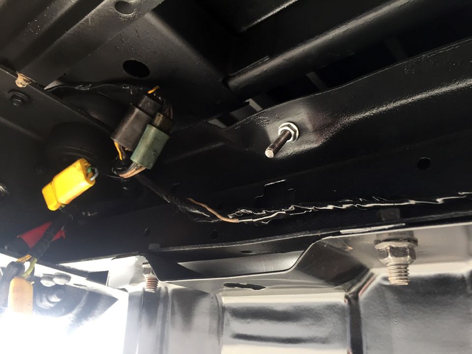Underbody view of black painted frame with wiring harness, connectors, and bolts