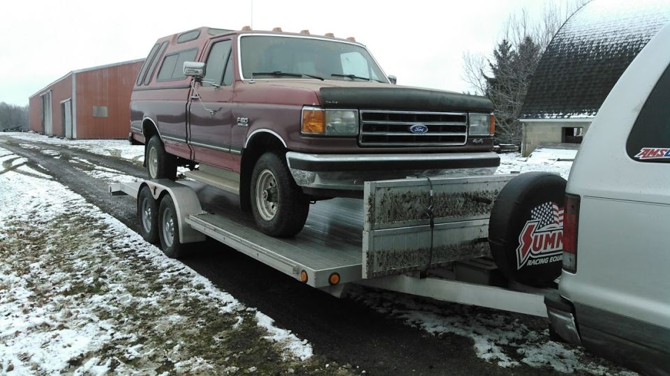 Maroon 1991 Ford F-150 with a camper shell on a trailer, being towed by another vehicle