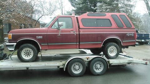 1991 Ford F-150 - A maroon Ford F-150 pickup truck with a red camper shell is being transported on a trailer.