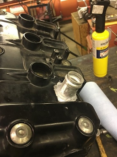 2000 Ford E350 - Close-up of a repaired engine valve cover with a torch and paper towels in the background.