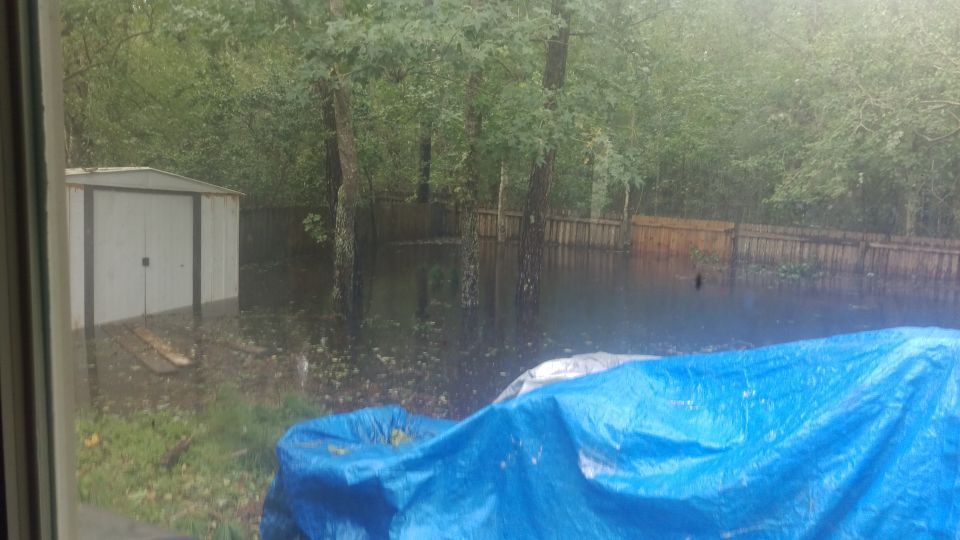 Flooded backyard with a shed and a blue tarp covering an unseen object