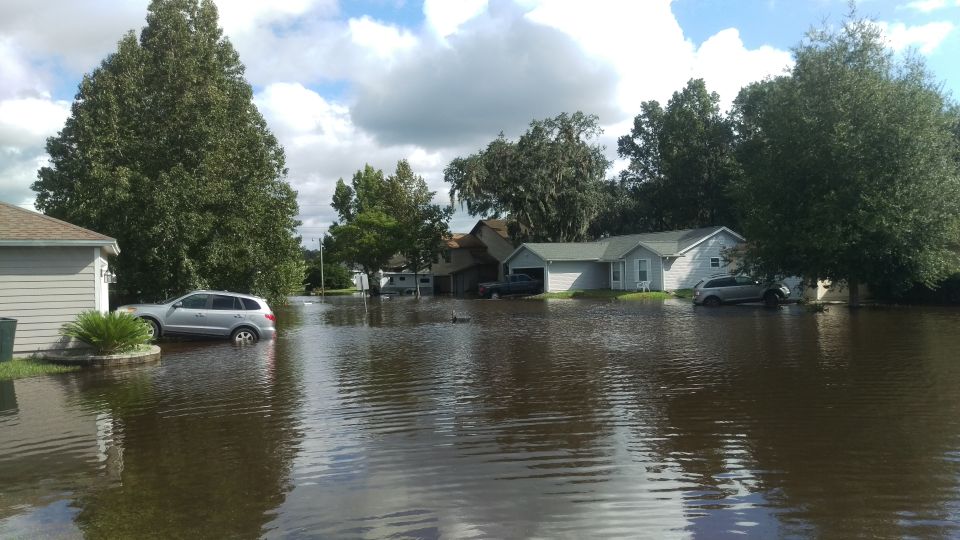 Silver SUV partially submerged in floodwaters next to a house