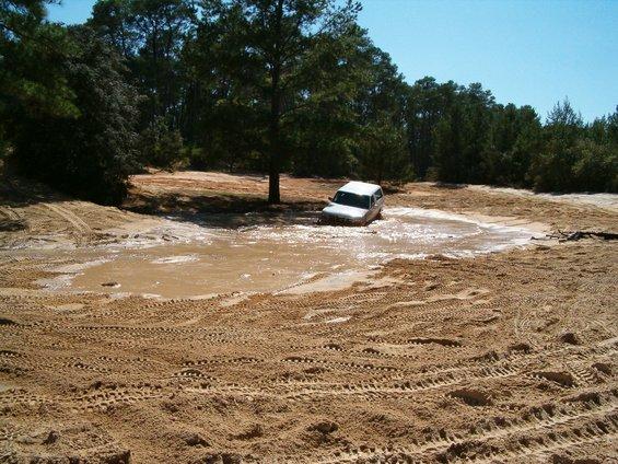 White full-size SUV wading through a brown mud pit at a sandy off-road park