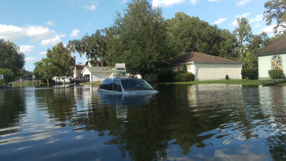 Silver minivan partially submerged in floodwaters, with a ladder on its roof