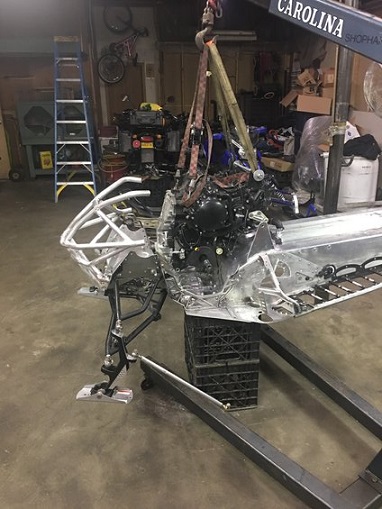 2000 Ford E350 - A snowmobile's engine and chassis are suspended by straps from a crane in a workshop.