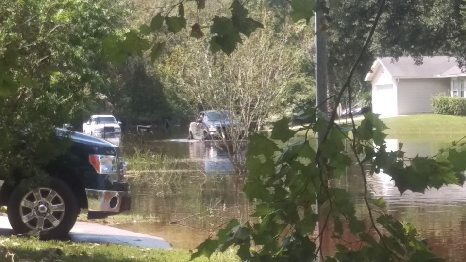 Flooded street with a black truck in the foreground and other vehicles submerged in water
