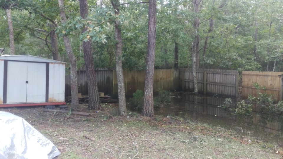 Flooded backyard with a white shed on the left and a wooden fence