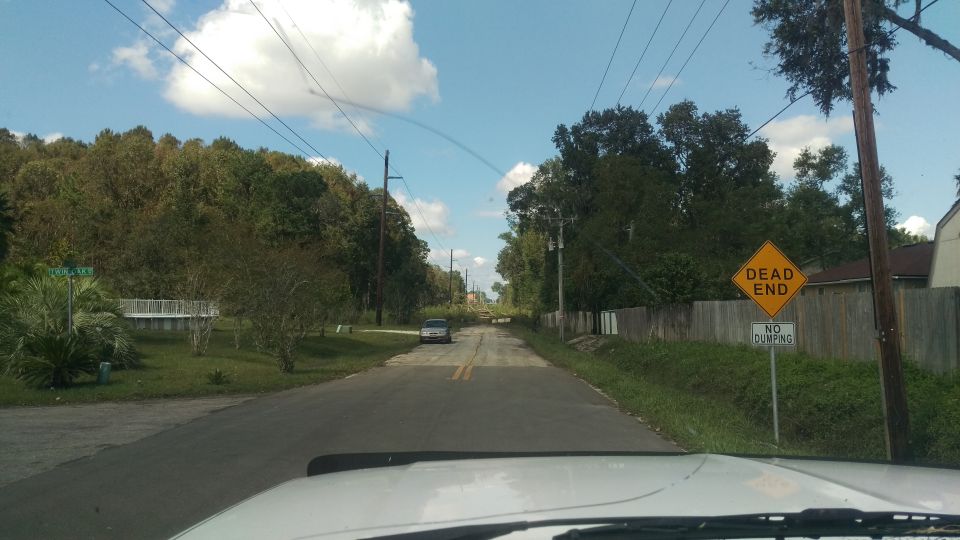 Driving down a road with trees and houses, a dead end sign is visible