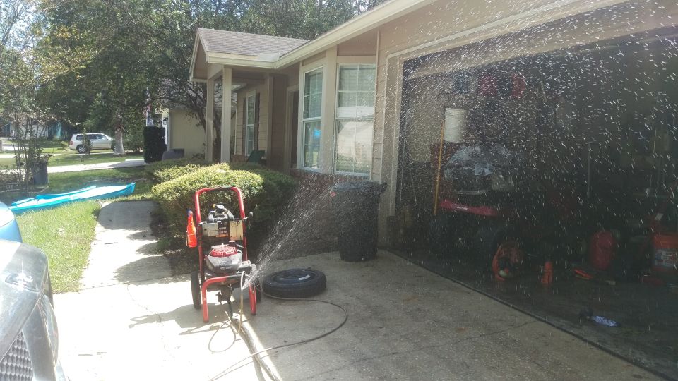 Pressure washer spraying water in front of a garage