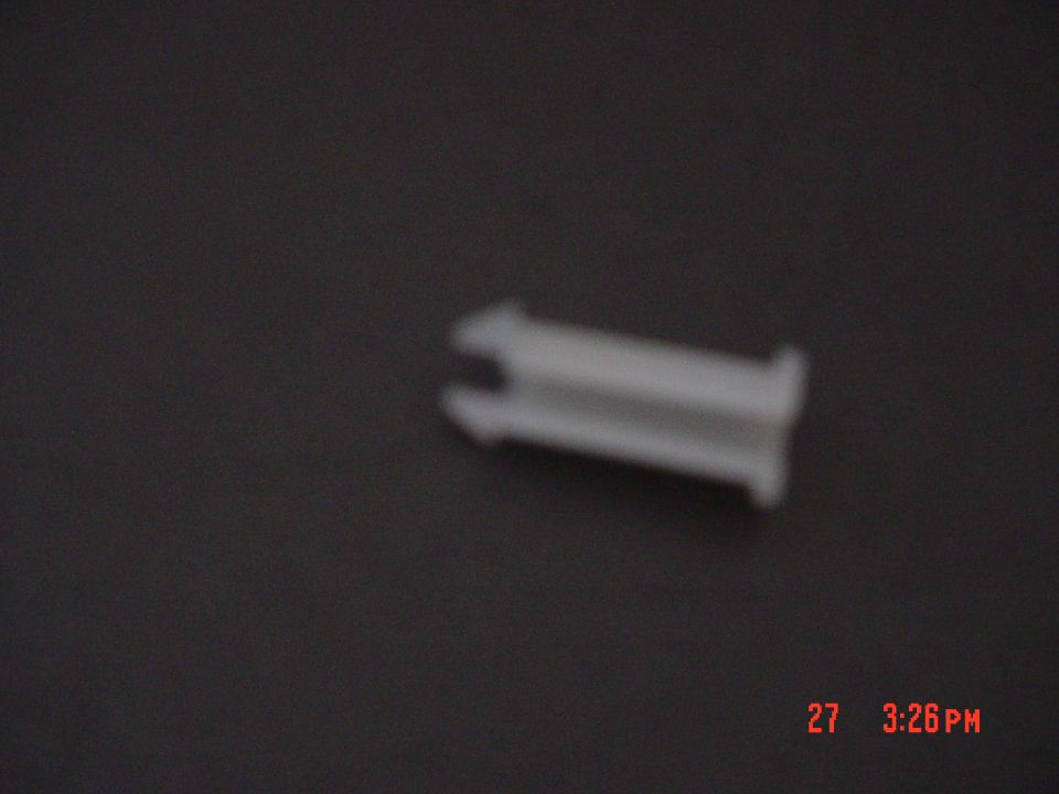 Small white plastic clip on a dark surface, blurry, with a red camera date stamp