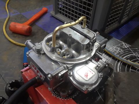 1985 Ford Bronco - A shiny chrome carburetor sits on a workbench, with a rubber mallet and yellow hose in the background.