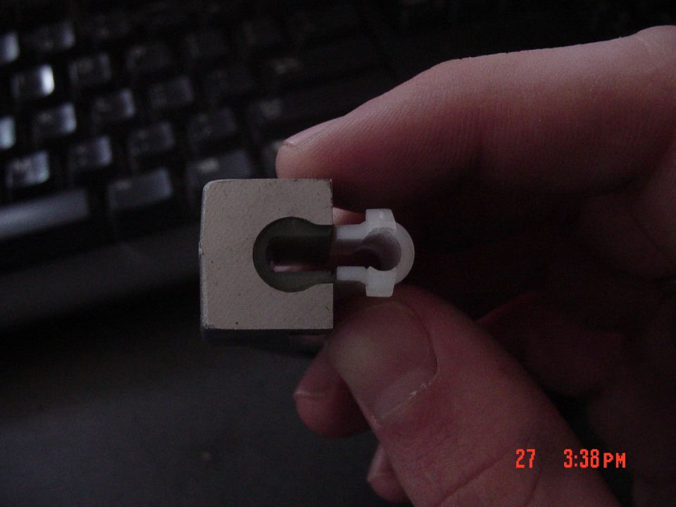Small metal block with keyhole-shaped slot and white plastic bushing held in a hand over a keyboard
