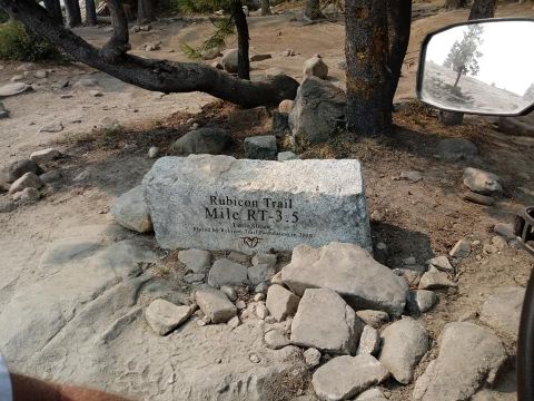 1979 Ford Bronco - A stone marker indicates the location on the Rubicon Trail, with a reflection of a tree in a vehicle's side mirror.