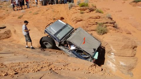 1979 Ford Bronco - An off-road vehicle is stuck in a deep sandy rut while onlookers observe from higher ground.