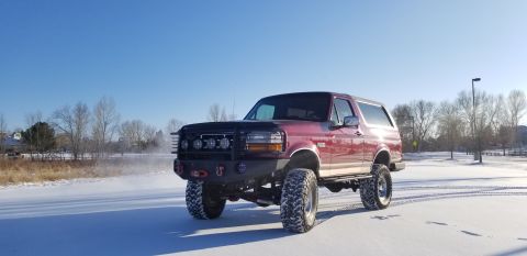 1996 Ford Bronco - A lifted red Ford Bronco sits on a snowy surface under a clear blue sky.