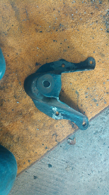 1978 Ford Bronco - A close-up view of a metal bracket with mounting holes, resting on a textured mat.