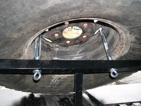 1986 Ford Bronco - Close-up view of a tire carrier mechanism, showing metal brackets securing a spare tire.