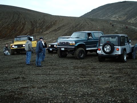 1996 Ford Bronco - A group of off-road vehicles, including a dark green Ford Bronco, are parked on a rocky terrain with hills in the background.