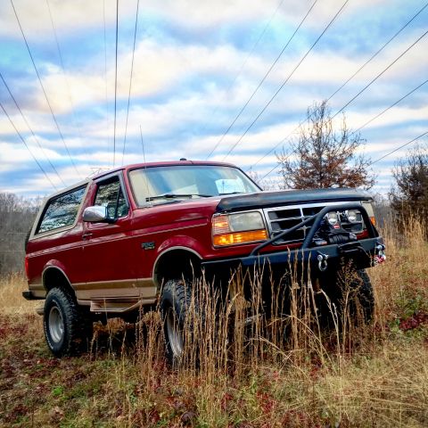 1995 Ford Bronco - Red 1995 Ford Bronco with aftermarket bumper and winch in a field.