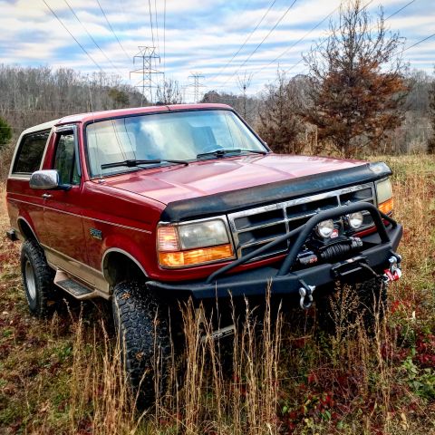 1995 Ford Bronco - This red Ford Bronco is equipped with a winch and aftermarket bumper, parked in a field under power lines.