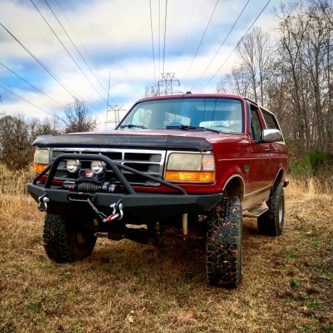 1995 Ford Bronco - This red Ford Bronco features an aftermarket bumper and winch, with a hood deflector protecting the front end.