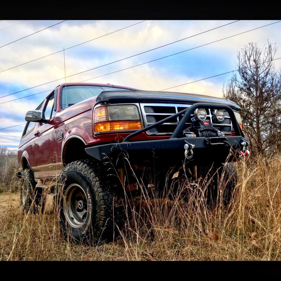 1995 Ford Bronco with custom front bumper, winch, and off-road tires parked in dry grass