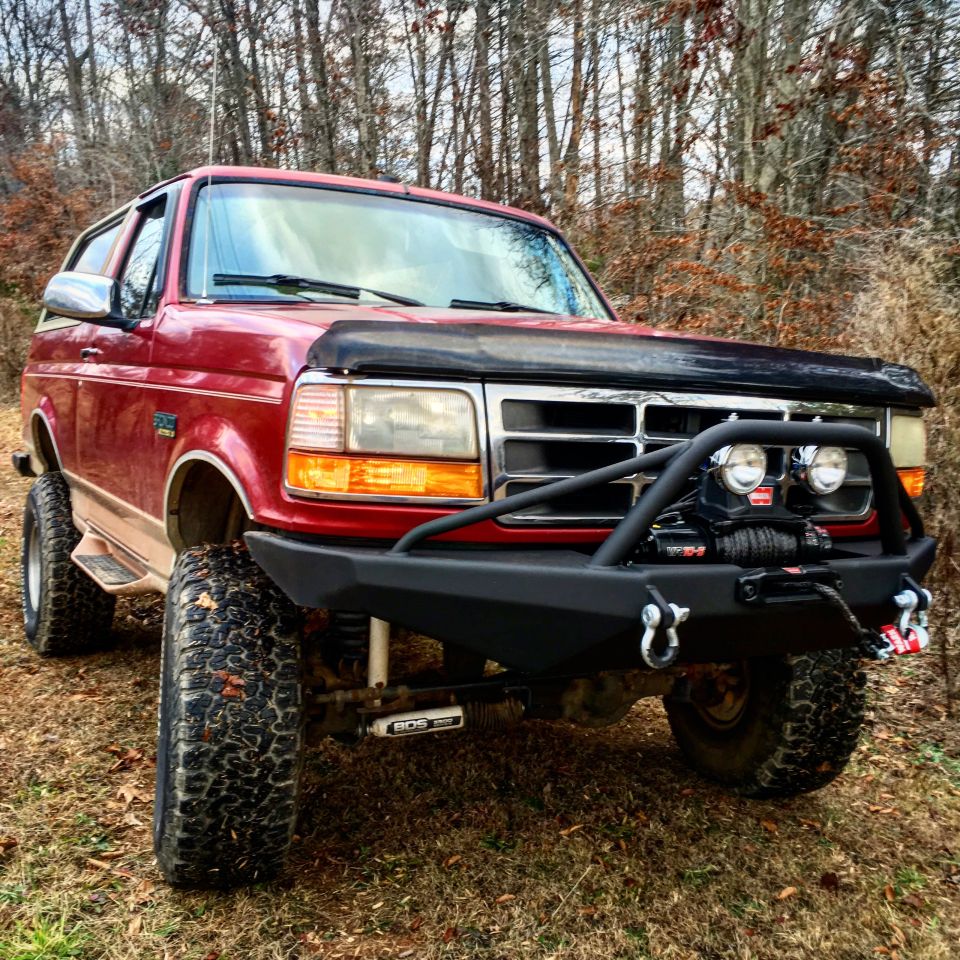 Red Ford Bronco with a black winch bumper and hood deflector, lifted on off-road tires