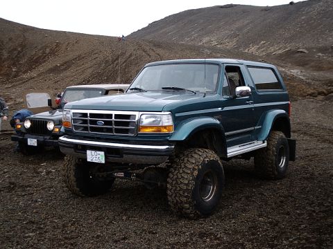 1996 Ford Bronco - A modified green Ford Bronco is parked on a rocky terrain, with a Jeep visible behind it.