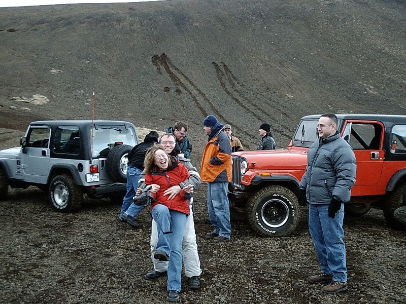 People and two Jeeps, silver and red, on gray volcanic gravel hillside