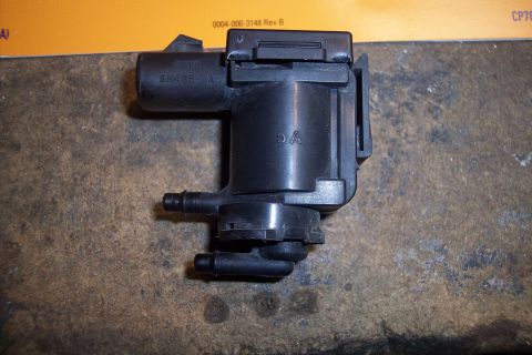 1995 Ford Bronco - A black plastic automotive part with visible hoses and markings is shown against a textured surface.