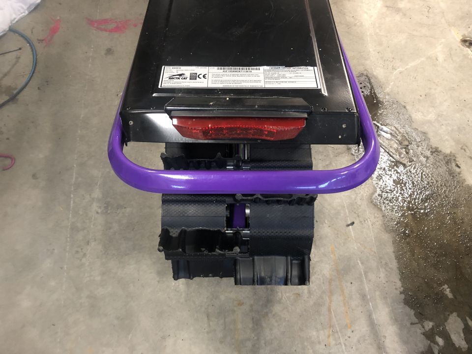 Snowmobile rear with purple handle, black track, and red taillight. Label on black surface