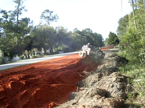 1985 Ford Bronco - Off-road vehicle navigates a steep, dusty incline next to a paved road.