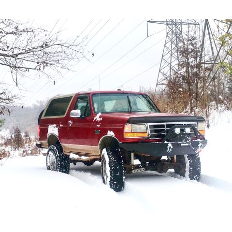 1995 Ford Bronco - This 1995 Ford Bronco navigates a snowy landscape, equipped with a heavy-duty aftermarket bumper and large off-road tires.