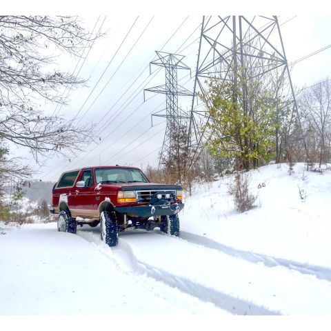 1995 Ford Bronco - Red 1995 Ford Bronco navigates a snow-covered path near power line towers.