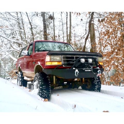 1995 Ford Bronco - A red 1995 Ford Bronco navigates a snowy path in a wooded area.