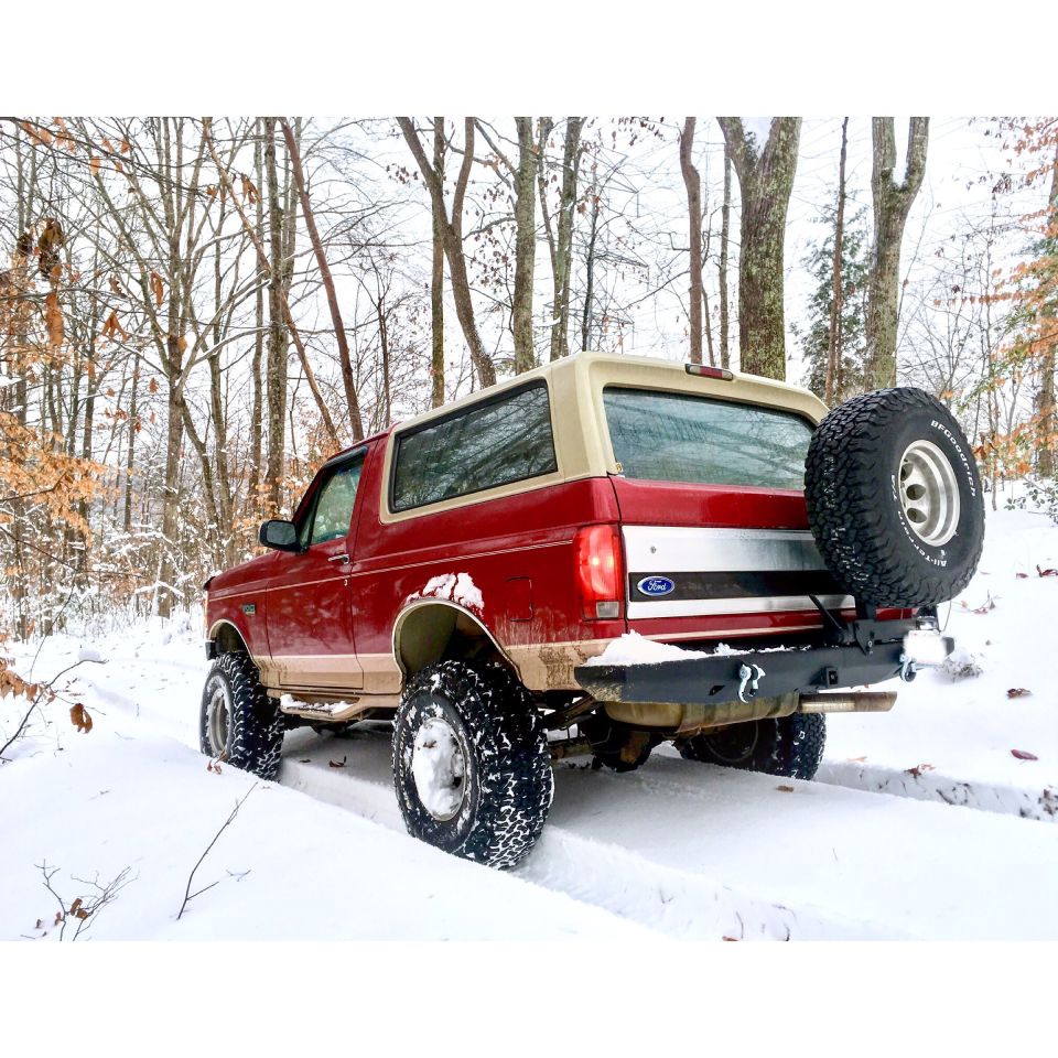 Red 1995 Ford Bronco with tan top and spare tire on rear bumper driving in snow