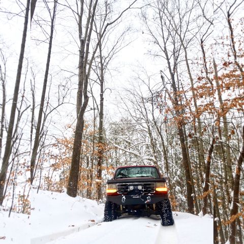 1995 Ford Bronco - A 1995 Ford Bronco navigates a snowy forest road, equipped with a winch and bumper.