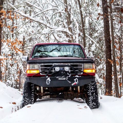 1995 Ford Bronco - A red Ford Bronco navigates a snowy forest path during winter.