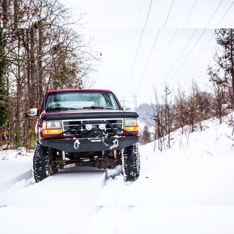 1995 Ford Bronco - A red Ford Bronco navigates through a snowy landscape with a custom bumper.